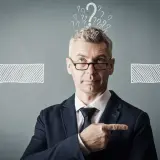 Un homme d'affaires réfléchit, entouré de points d'interrogation et de flèches. Il cherche la meilleure solution, peut-être avec un logiciel GED.