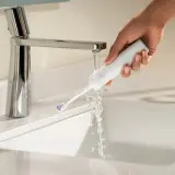 Mano che sciacqua uno spazzolino elettrico sotto un rubinetto. Ideale per chi soffre di gengive ritirate.