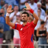 Novak Djoković w czerwonej koszulce z podniesionymi rękami, pozdrawia publiczność po zwycięstwie w turnieju WTA 500.