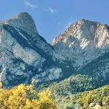 Majestuosas montañas de el Pedraforca bajo un cielo azul. El sol ilumina las cumbres rocosas y los bosques verdes.