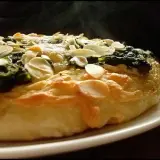 Eine köstliche Spinat Pizza mit knusprigem Teig und gerösteten Mandelblättchen. Dampf steigt auf und verspricht ein warmes, herzhaftes Gericht.