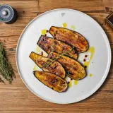 Gegrillte Auberginenscheiben als Antipasti, beträufelt mit Olivenöl und Balsamico, garniert mit Thymian.