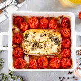 Feta in friggitrice ad aria, circondata da pomodorini arrostiti, aglio e erbe aromatiche. Un piatto semplice e gustoso.