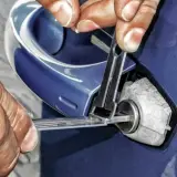 Manos expertas intentan abrir coche sin llave con herramientas especializadas.