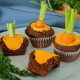 Schokoladen-Muffins mit orangefarbener Glasur und einem kleinen Karottenstück mit Grün als Osterdekoration.