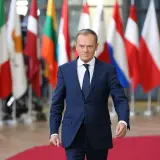 Donald Tusk, z niemieckim pochodzeniem, idzie na tle flag UE.