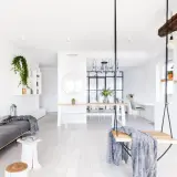 Jasny salon z białymi ścianami, szarą kanapą, huśtawką i stołem jadalnianym.