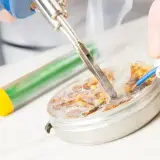 Precyzyjne lutowanie przewodu z użyciem cyny i rozgrzanej lutownicy. Dym unosi się nad pracą.