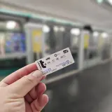 Dłoń trzyma bilet na metro paryskie. W tle widać pociąg metra.