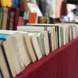Rząd książek na czerwonym obrusie. Jak przygotować się do targów książki jako autor i czytelnik?