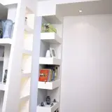 Scaffali moderni in cartongesso, con libri, vasi e soprammobili, creano un angolo lettura accogliente.