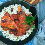 Un plat de poulet sauce tomate savoureux, servi sur un lit de riz blanc, garni d'olives noires et de persil frais.