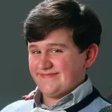 Uśmiechnięty Dudley Dursley, kuzyn Harry'ego Pottera, w niebieskim swetrze.