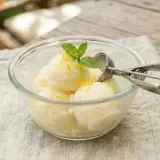 Un délicieux sorbet citron sans sorbetière, garni de menthe fraîche et de zestes de citron, servi dans un bol en verre.