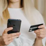 Kobieta z blond włosami trzyma telefon i kartę płatniczą, szukając informacji, jak zwiekszyc limit PayPo.
