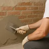 Man con guantes aplica revoque a pared de ladrillos, un paso clave para saber como quitar la humedad para siempre.