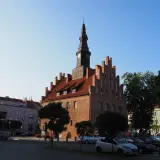 Ratusz w mieście nad jeziorem Skiertąg, z charakterystyczną wieżą zegarową, otoczony kolorowymi kamienicami i zielenią.
