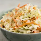 En skål med krämig, krispig coleslaw med strimlad vitkål och morötter, toppad med svartpeppar. Perfekt som tillbehör till grillat, detta är den godaste coleslaw!
