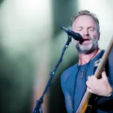Sting, wokalista The Police, gra na gitarze basowej i śpiewa do mikrofonu na koncercie.