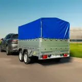 Samochód holuje przyczepkę z niebieską plandeką. Dowiedz się, jak zarejestrować przyczepkę, by podróżować bezpiecznie.
