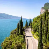 Route panoramique longeant un lac italien, idéale pour le camping-car. Cyprès élancés, falaises et eau bleue invitent à l'aventure.