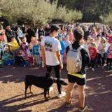 Un grupo de personas, incluyendo niños, se reúne en un sendero boscoso. Un hombre con una camiseta roja toma una foto con su móvil. Un perro Dóberman negro está atado a un joven. Quizás están buscando al **dragón de la Calderona**.