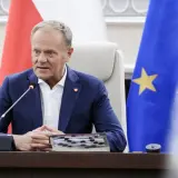 Donald Tusk w Sosnowcu, przemawia przy mikrofonie, za nim flagi Polski i UE.