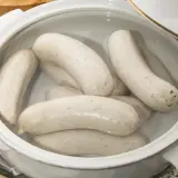 Kilka białych kiełbasek parzonych w garnku, gotowych do podania.