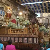 Procesión religiosa con un elaborado trono de madera adornado con flores y figuras. El **corpus 2026** se prepara para la festividad.