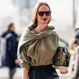 Mujer de unos 40 años con un look casual chic, gafas de sol, suéter gris y bolso estampado.