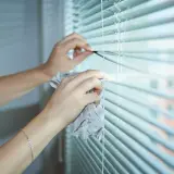 Ręce czyszczą żaluzje fasadowe wilgotną ściereczką, usuwając kurz i przywracając im blask.