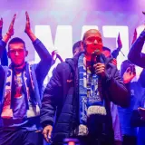 Mężczyzna z mikrofonem, otoczony przez młodych ludzi w szalikach, świętuje sukces jako mistrz polski ekstraklasa.