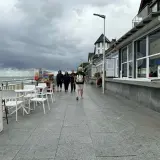 Spacer w Sarbinowie, gdy pada. Ludzie idą promenadą obok barów z lodami i kawiarni, szukając atrakcji.