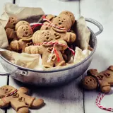 Un cuenco lleno de galletas de jengibre con forma de hombrecito, algunas atadas con hilo rojo y blanco.