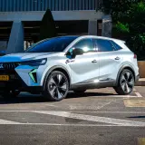 Nowy Mitsubishi Grandis w białym kolorze, zaparkowany na parkingu przed budynkiem.