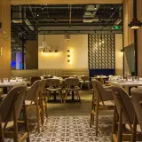 Przytulne wnętrze restauracji z drewnianymi panelami i stylowym oświetleniem. Stoliki nakryte, gotowe na gości.