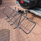 Czarny, metalowy uchwyt do przewozu motocykla na hak, gotowy do montażu przy samochodzie.