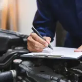 Mechanik spisuje protokół przeglądu samochodu po terminie, notując stan techniczny pojazdu.