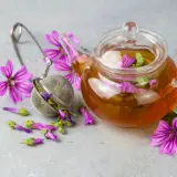Tè alla malva in teiera di vetro, con fiori e infusore. Attenzione ai malva effetti collaterali.