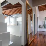 Specchio dorato e cactus per rendere luminoso un corridoio moderno con soffitto a vista in legno.