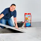 Instalador coloca baldosa sobre adhesivo. Bolsa de Pegacor y herramientas, para saber como se calcula la superficie.