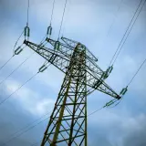 Wysoki słup energetyczny z przewodami, pod niebem pełnym chmur. Mam nadzieję, że nie będzie awarii, bo wtedy czeka nas bonifikata za brak prądu.