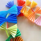 Kolorowy łańcuch choinkowy z papieru, wykonany techniką origami. Wesołe ozdoby w kształcie wachlarzy i kokardek.