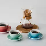 Chemex vs drip: trzy kolorowe filiżanki z kawą i szklany dzbanek Chemex na drewnianej podstawce.