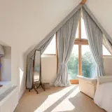 Graue Vorhänge rahmen ein Dreiecksfenster ein und lassen viel Licht herein. Sie sind elegant mit Bändern befestigt.