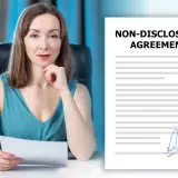 Kobieta w biurze trzyma dokument. Obok widoczny jest podpisany dokument "Non-Disclosure Agreement", czyli umowa o zachowanie poufności.