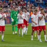 Piłkarze w białych strojach z orzełkiem na piersi, być może przyszli mistrzowie polski w piłce nożnej, stoją na murawie.