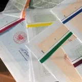 Stos papierów z kolorowymi wstążkami, każdy z pieczęcią i podpisem dyrektora. To świadectwo ukończenia szkoły.