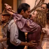 Una coppia balla stretta, immersa in un'atmosfera festosa. La scena evoca un'epoca passata, quasi una spiegazione visiva di un ballo di Babylon.