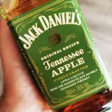 Dłoń trzyma butelkę Jack Daniel's Tennessee Apple. Ten miodowy likier jabłkowy to idealny dodatek do wieczoru.
